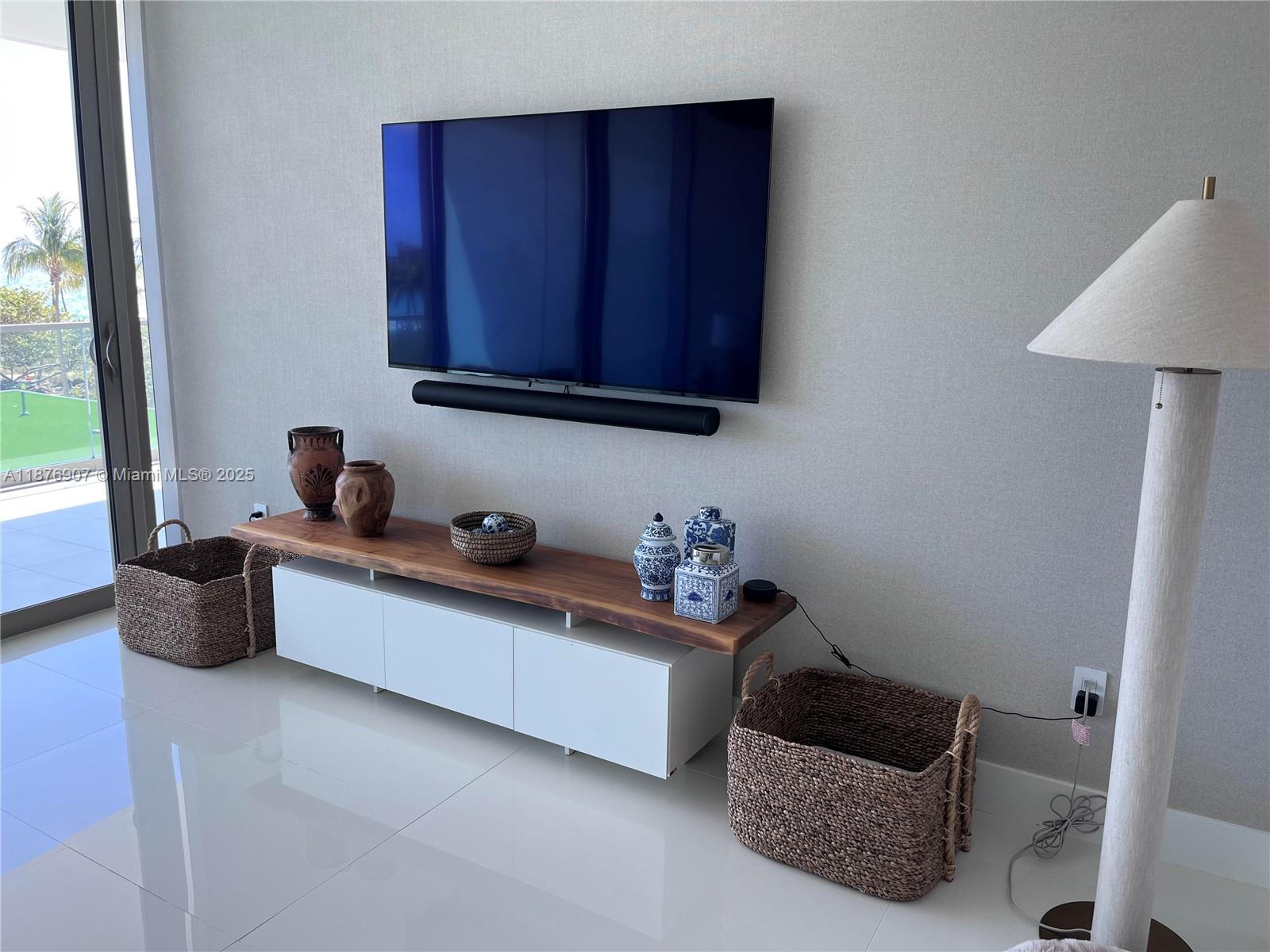 A living room features a wall-mounted television, a wooden media console, and two woven baskets — 10201 Collins Ave # 301, Bal Harbour FL 33154, BAL HARBOUR, FL