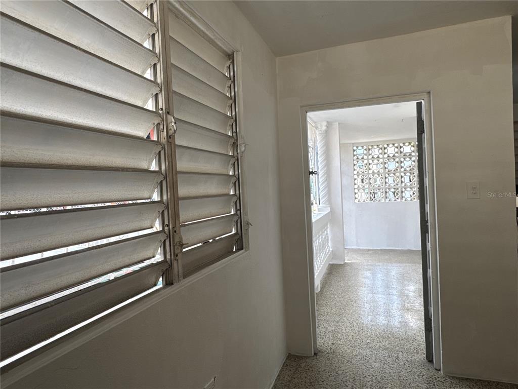 A room with louvered windows leads through a doorway to a sunroom with breeze blocks — 121 CALLE HERMANDAD INTERIOR, GUAYNABO, PR