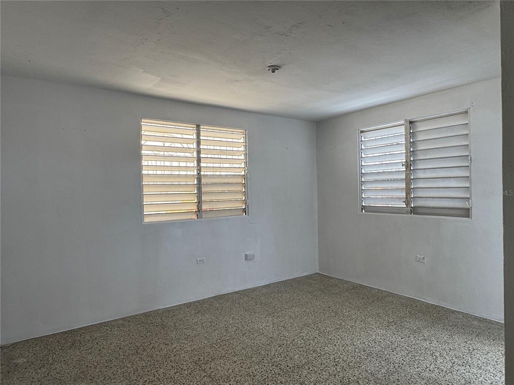 An empty room with white walls, two louvered windows, and speckled tile flooring — 121 CALLE HERMANDAD INTERIOR, GUAYNABO, PR