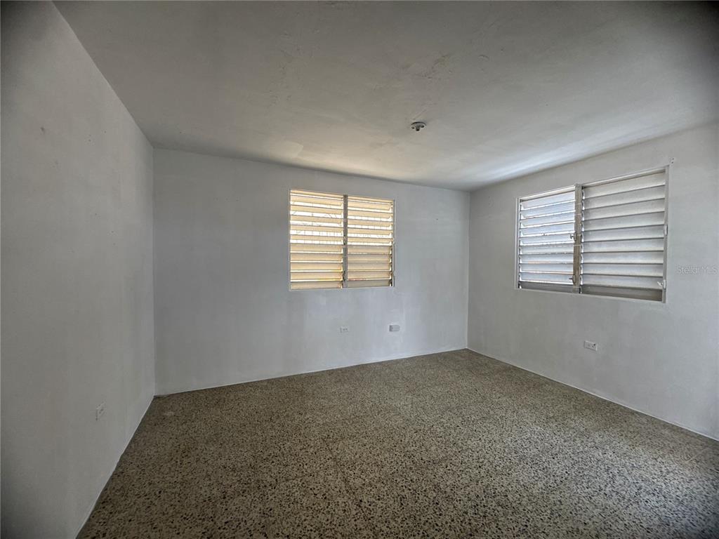 An empty room with white walls, a speckled floor, and two windows with louvered shutters — 121 CALLE HERMANDAD INTERIOR, GUAYNABO, PR