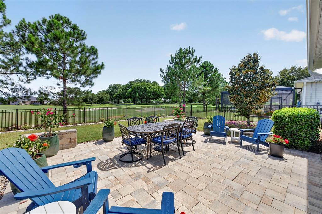 A paved patio features a dining set and blue Adirondack chairs overlooking a golf course — 5448 NW 35TH LANE ROAD, OCALA, FL
