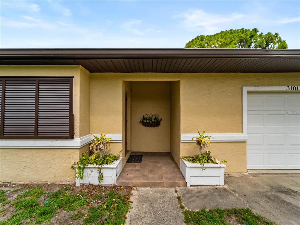 The exterior of a house features a tan stucco facade, a garage, and two planters — 3181 NORMANDY DRIVE, PORT CHARLOTTE, FL