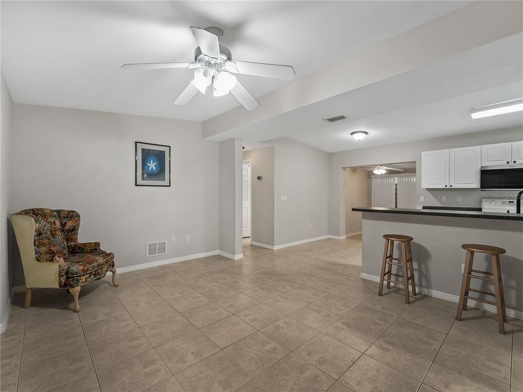 A tiled living area features a floral armchair, a ceiling fan, and an open kitchen — 3181 NORMANDY DRIVE, PORT CHARLOTTE, FL
