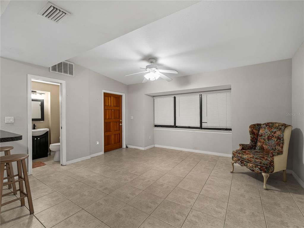A room with tile flooring, a ceiling fan, a wooden door, and a floral armchair — 3181 NORMANDY DRIVE, PORT CHARLOTTE, FL