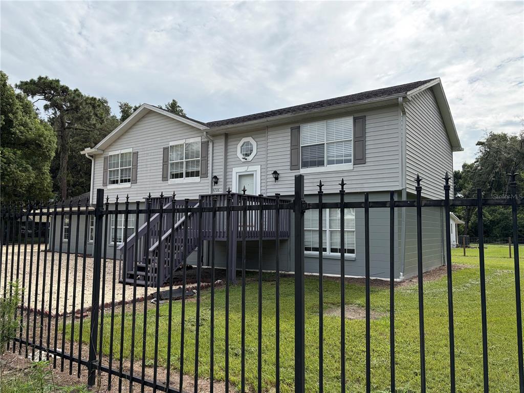 A two-story house with gray siding and a black metal fence in the foreground — 4706 COATS ROAD, ZEPHYRHILLS, FL