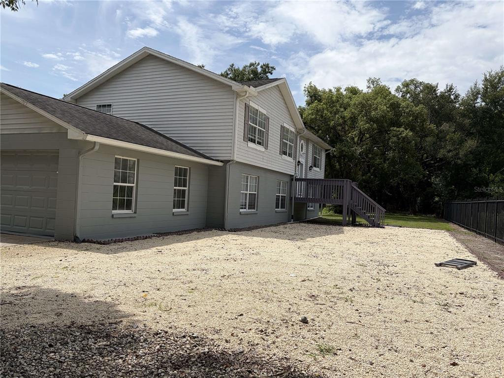 A two-story house with gray siding and a gravel yard features a wooden deck — 4706 COATS ROAD, ZEPHYRHILLS, FL