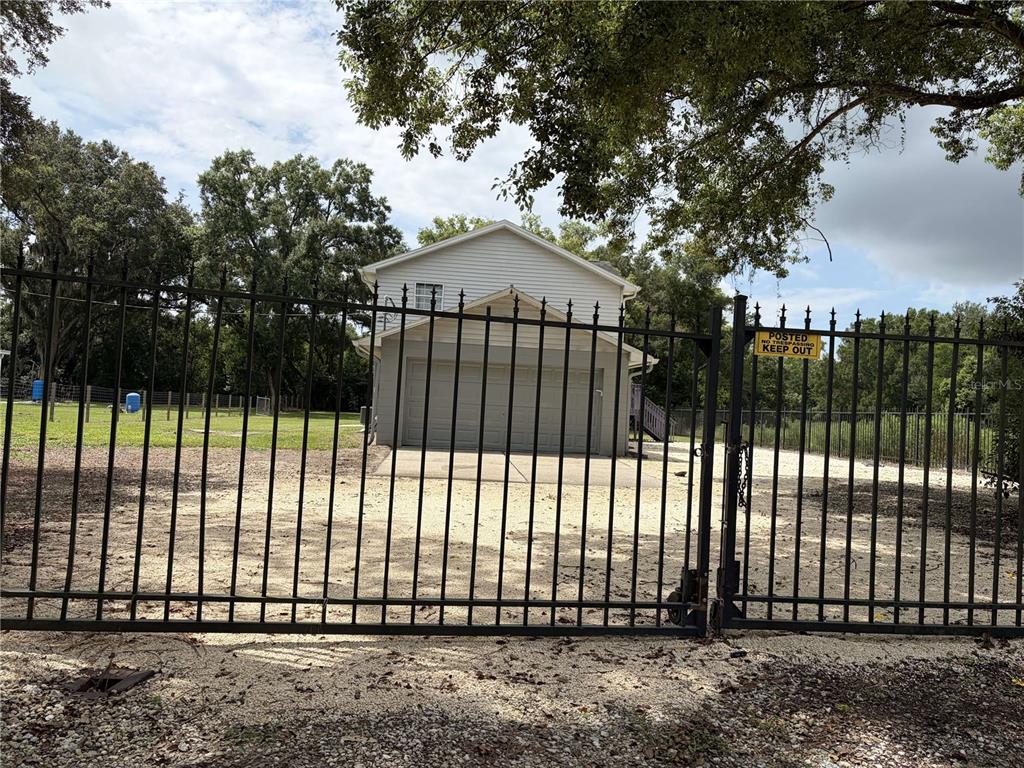 A two-story house with a garage is viewed through a closed black metal gate — 4706 COATS ROAD, ZEPHYRHILLS, FL