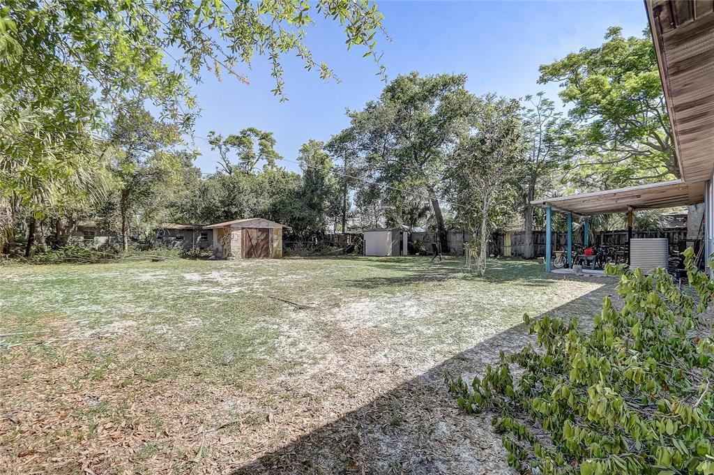 A large, grassy backyard features a wooden shed, a covered patio, and mature trees — 243 W MARTIN STREET, APOPKA, FL