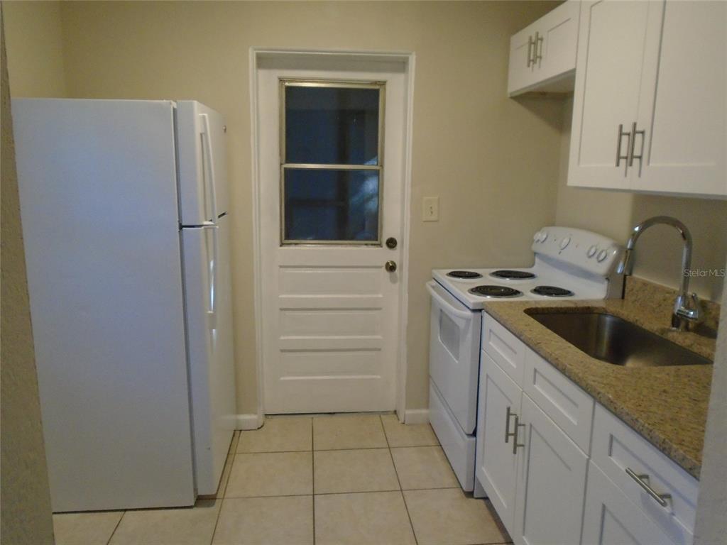 A small kitchen features white appliances, light-colored cabinets, a granite countertop, and tile flooring — 131 LEMON LANE, CASSELBERRY, FL