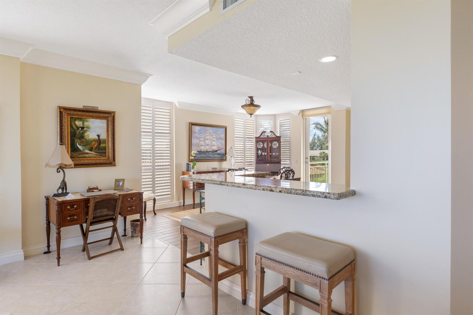 A kitchen breakfast bar with two stools overlooks a living area with a desk — HUTCHINSON ISLAND, FL