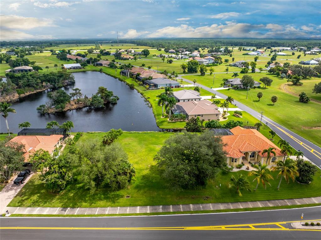 An aerial view shows a vacant grassy lot situated between two houses near a pond — 17204 CAPE HORN BOULEVARD, PUNTA GORDA, FL