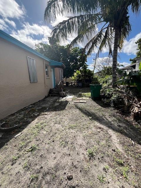 A side yard of a house with a palm tree, dirt ground, and a green bin — 2956 NW 49th Street, Miami FL 33142, MIAMI, FL