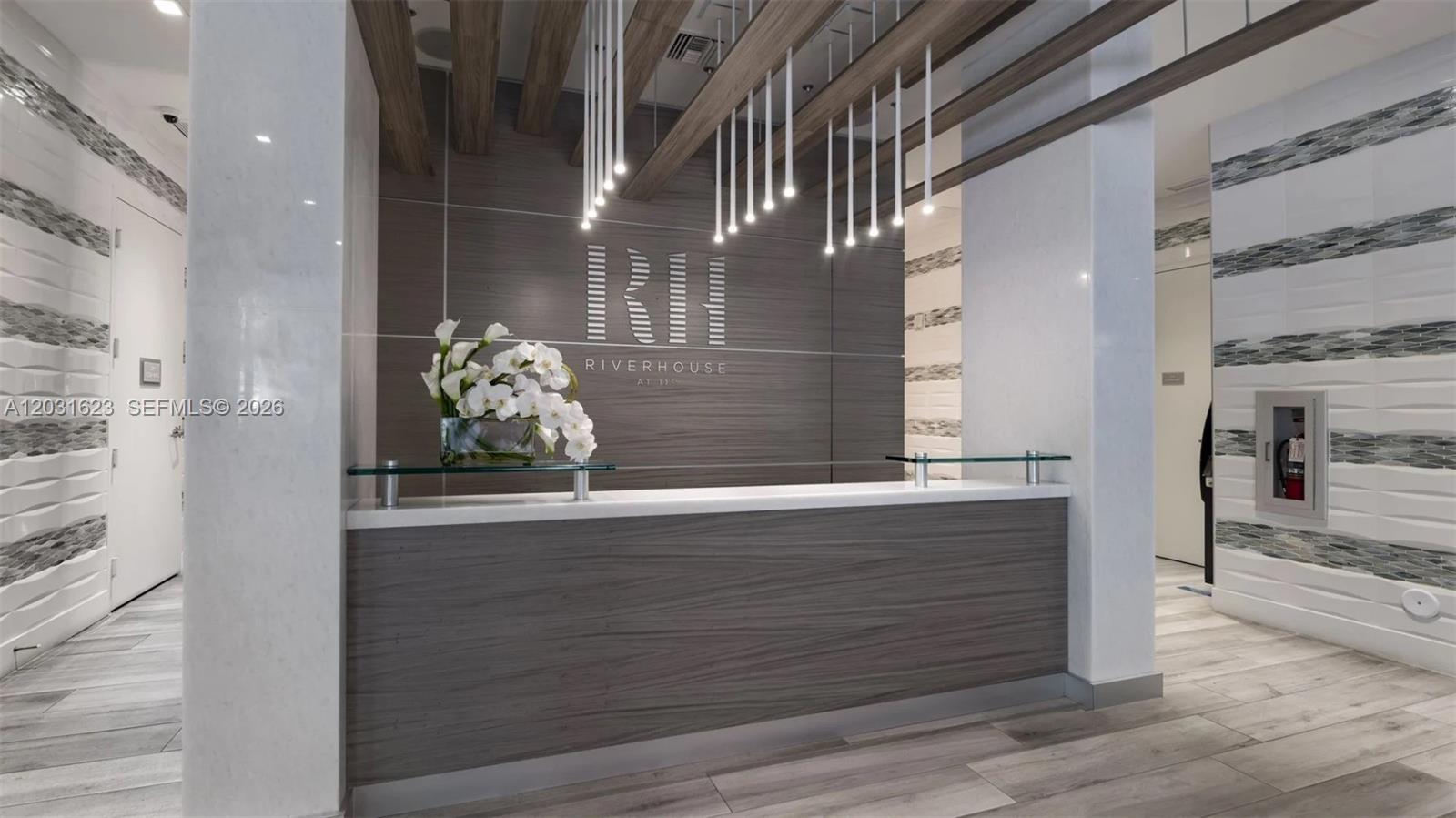 A modern reception desk with a wood-grain front sits in a lobby with pendant lighting — 1170 NW 11th St # 704, Miami FL 33136, MIAMI, FL