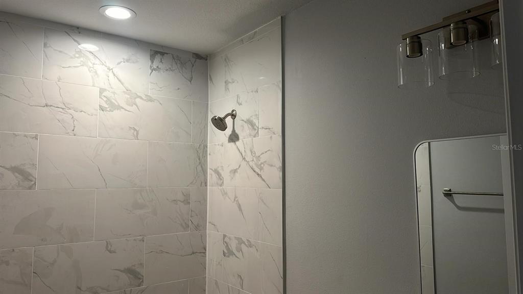 A bathroom features a marble-tiled shower, a wall-mounted mirror, and a modern light fixture — 12231 KIRK AVENUE UNIT 2, PORT CHARLOTTE, FL