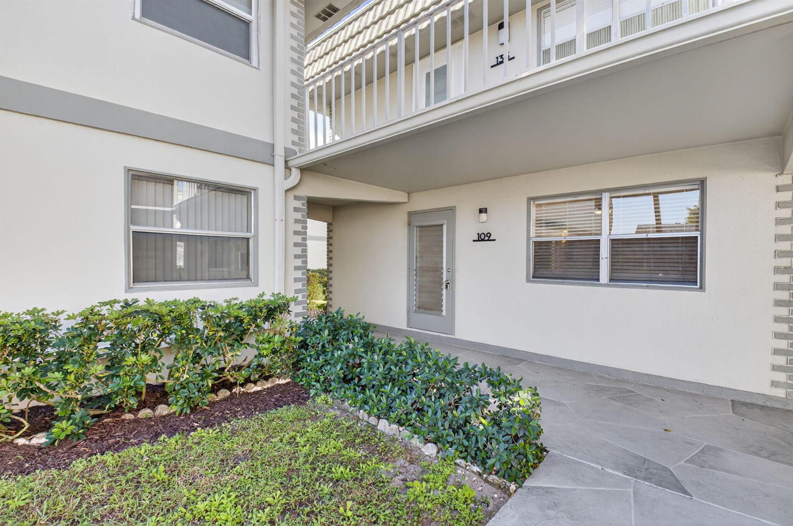 The exterior of a ground-floor apartment entrance features a stone patio and green landscaping — 109 Monaco C # 109, Delray Beach FL 33446, DELRAY BEACH, FL