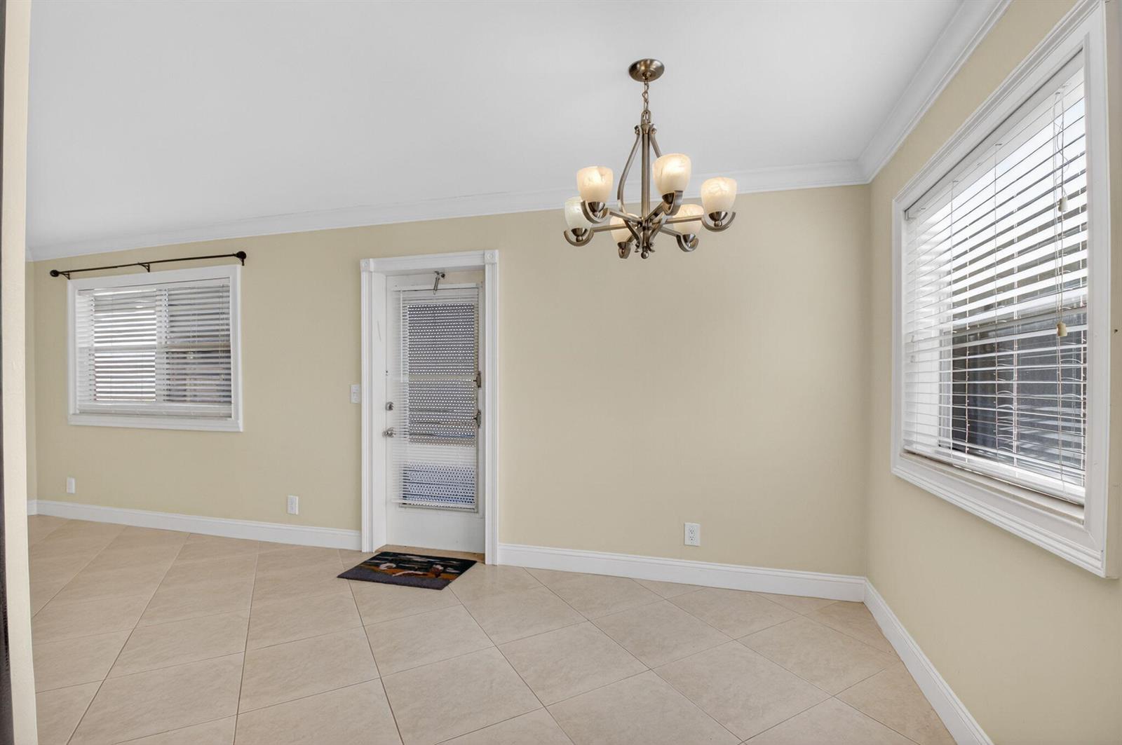 An empty room with beige walls, tile flooring, a chandelier, and two windows with blinds — 109 Monaco C # 109, Delray Beach FL 33446, DELRAY BEACH, FL