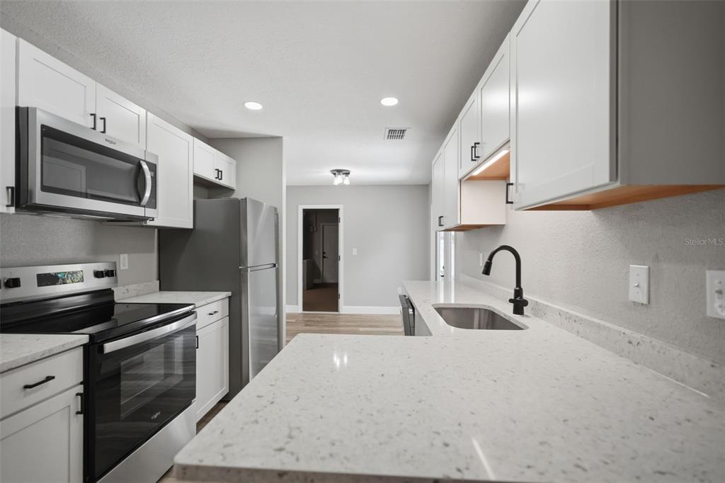 A modern kitchen features white cabinets, stainless steel appliances, and light-colored quartz countertops — 7407 DUNDEE WAY, WEEKI WACHEE, FL