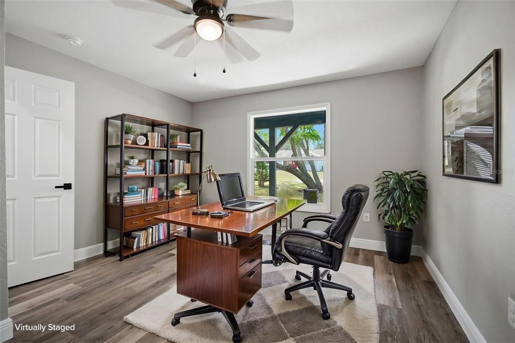 A home office features a wooden desk, a black chair, and a bookshelf on wood flooring — 7407 DUNDEE WAY, WEEKI WACHEE, FL