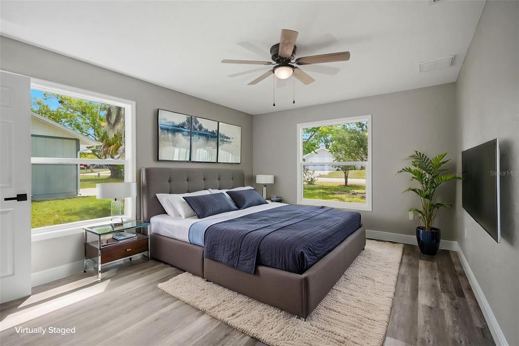 A bedroom features a gray upholstered bed, wood-look flooring, and a ceiling fan — 7407 DUNDEE WAY, WEEKI WACHEE, FL