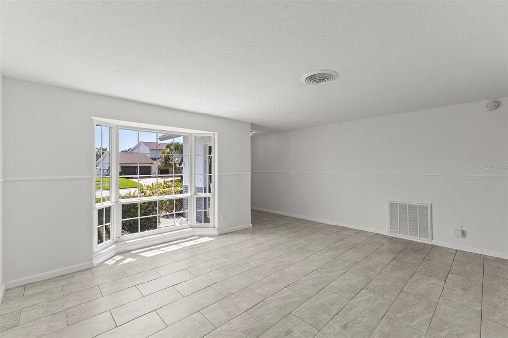 A bright, empty room features light-colored tile flooring, white walls, and a large bay window — 4960 DOVER STREET NE, ST PETERSBURG, FL