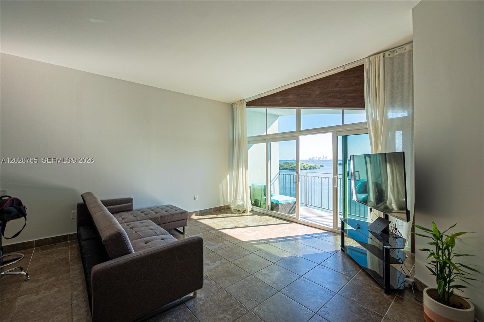A living room features tile floors, a gray sectional sofa, and floor-to-ceiling windows with water views — 770 NE 69th St # 8F, Miami FL 33138, MIAMI, FL