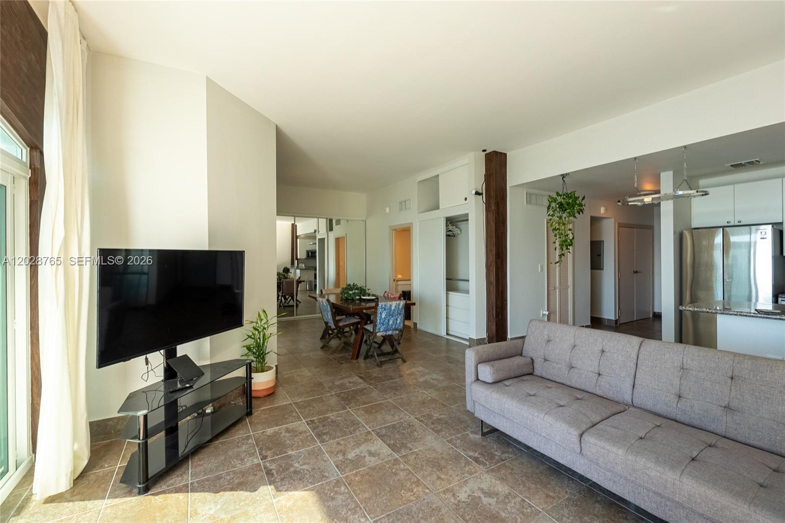 A living room with tile floors, a grey sofa, a television, and an open kitchen — 770 NE 69th St # 8F, Miami FL 33138, MIAMI, FL