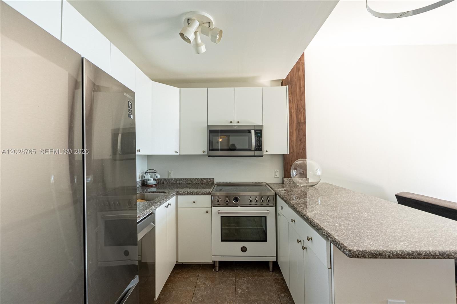 A kitchen features white cabinets, granite countertops, stainless steel appliances, and a tile floor — 770 NE 69th St # 8F, Miami FL 33138, MIAMI, FL