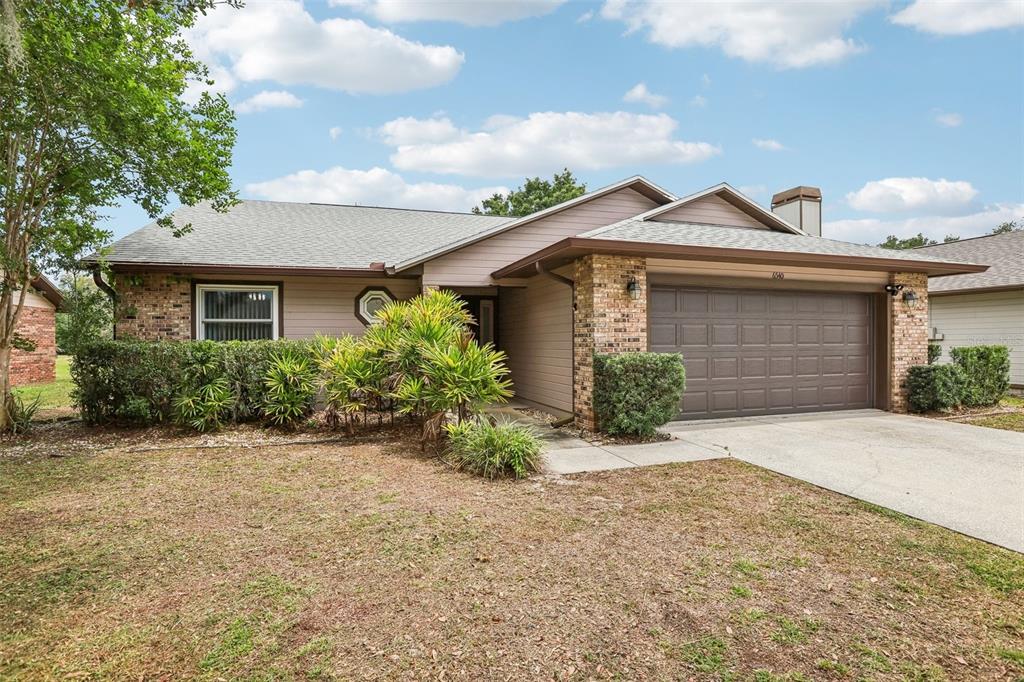 A single-story house with tan siding, brick accents, a two-car garage, and mature landscaping — 6540 FOXMOOR DRIVE, ZEPHYRHILLS, FL