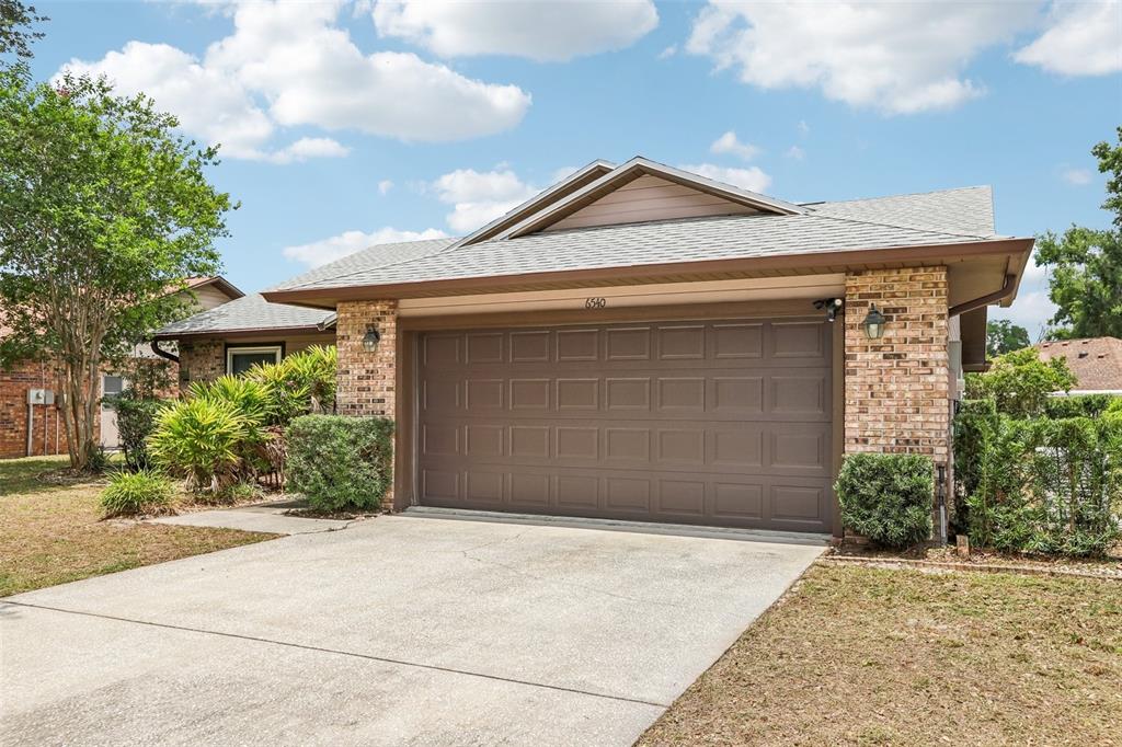 A single-story house with a brown garage door, brick accents, and a front lawn — 6540 FOXMOOR DRIVE, ZEPHYRHILLS, FL