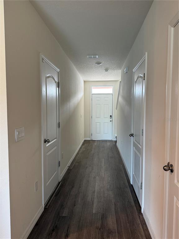 A narrow hallway with wood-look flooring leads to a white front door — 1217 BALSAM DRIVE, DAVENPORT, FL