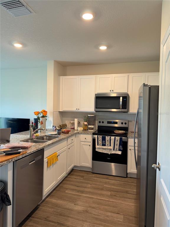 A kitchen with white cabinets, stainless steel appliances, and wood-look flooring — 1217 BALSAM DRIVE, DAVENPORT, FL