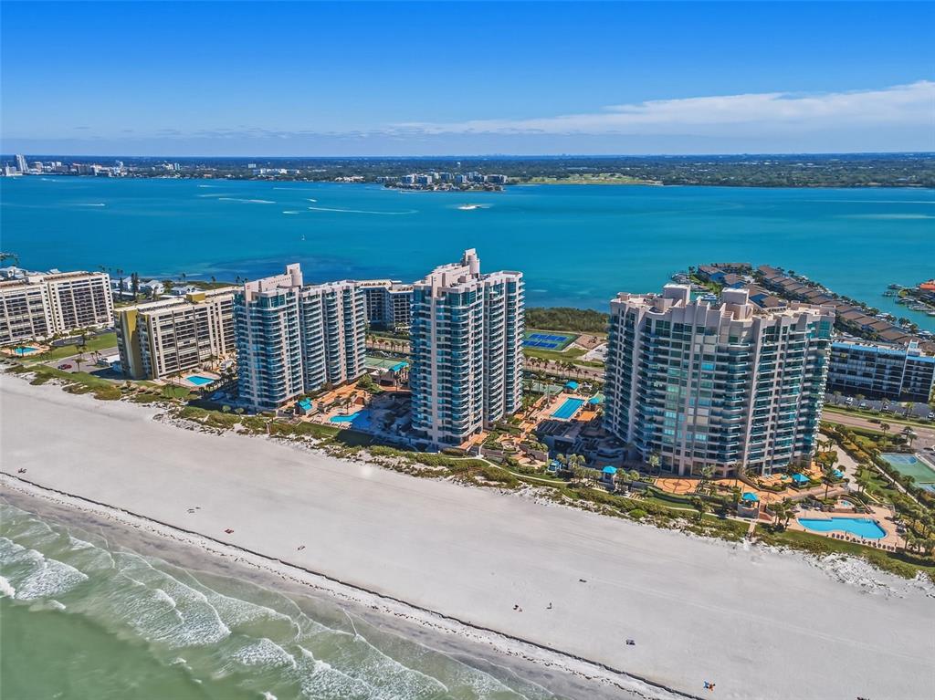 An aerial view shows several high-rise residential buildings situated along a sandy beach and ocean — 1540 GULF BOULEVARD UNIT 1004, CLEARWATER BEACH, FL