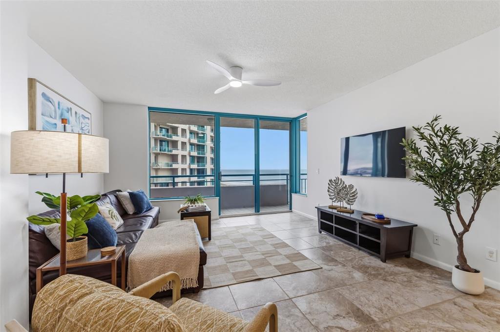 A living room features tile floors, a ceiling fan, a balcony with ocean views, and furniture — 1540 GULF BOULEVARD UNIT 1004, CLEARWATER BEACH, FL