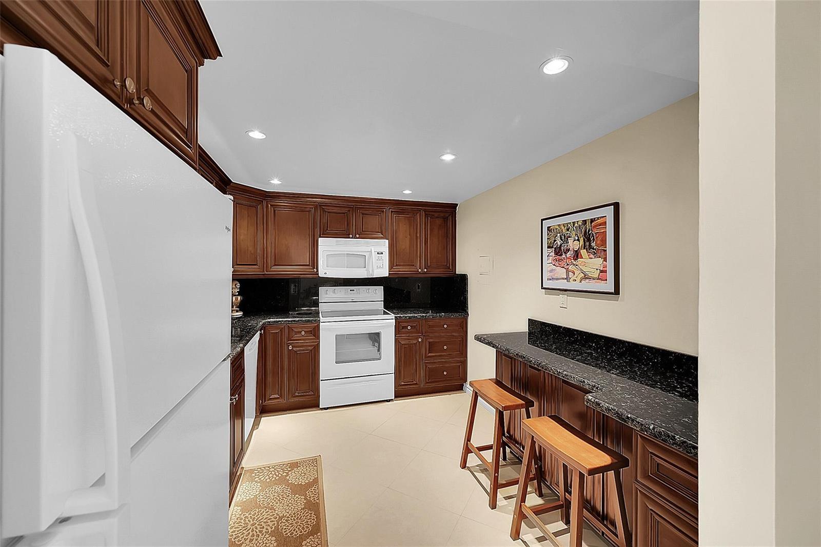 A kitchen features dark wood cabinets, black granite countertops, white appliances, and a breakfast bar — 531 N Ocean Boulevard # 410, Pompano Beach FL 33062, POMPANO BEACH, FL