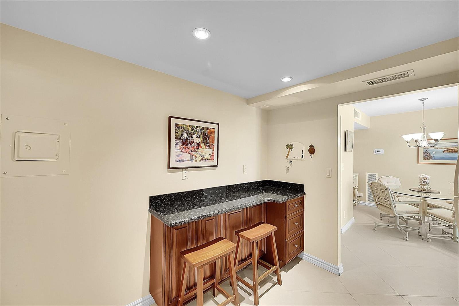 A wet bar with dark wood cabinets and granite countertops sits against a beige wall — 531 N Ocean Boulevard # 410, Pompano Beach FL 33062, POMPANO BEACH, FL