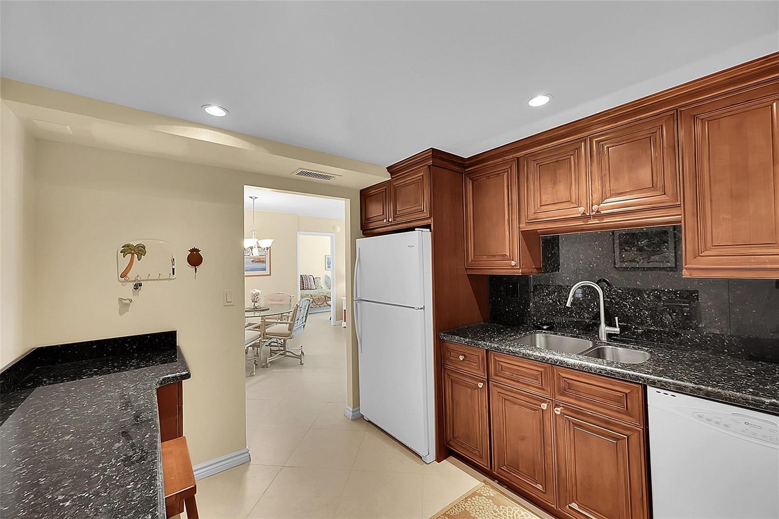 A kitchen features wood cabinets, black granite countertops, a white refrigerator, and a double sink — 531 N Ocean Boulevard # 410, Pompano Beach FL 33062, POMPANO BEACH, FL