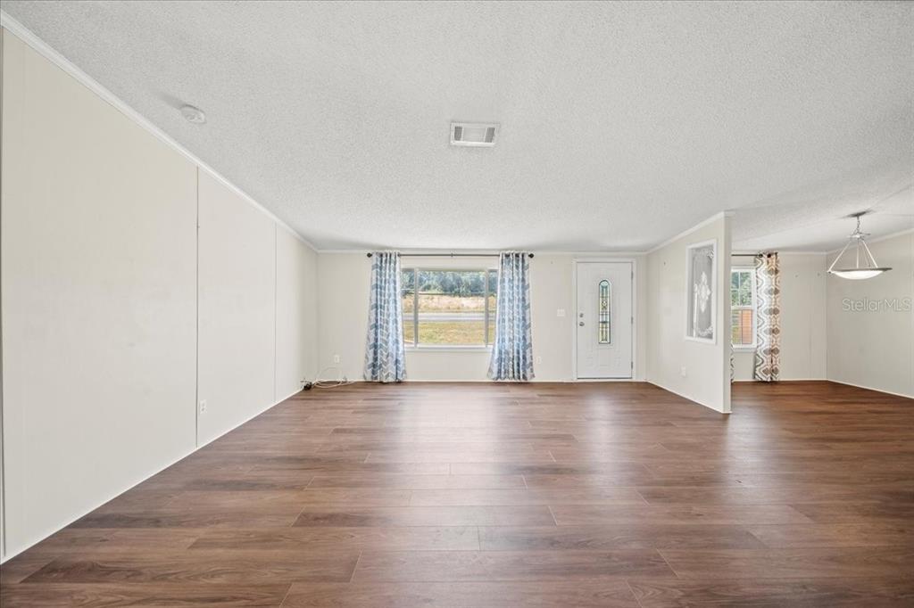 A spacious living room features wood-look flooring, white walls, and a large front window — 101 EDGEWOOD BOULEVARD, LAKE WALES, FL