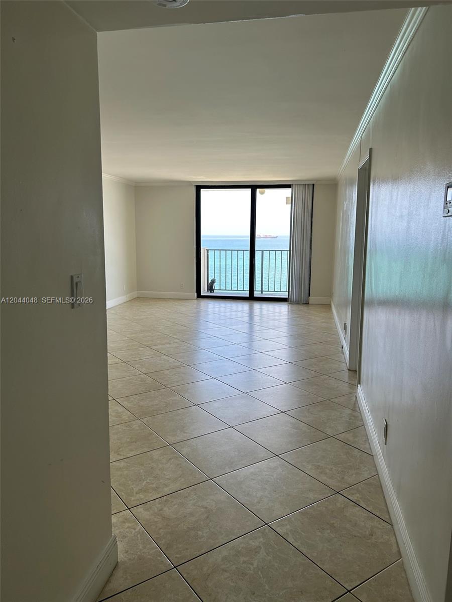 An empty room with beige tile flooring leads to a balcony overlooking the ocean — 2625 Collins Ave # 1805, Miami Beach FL 33140, MIAMI BEACH, FL