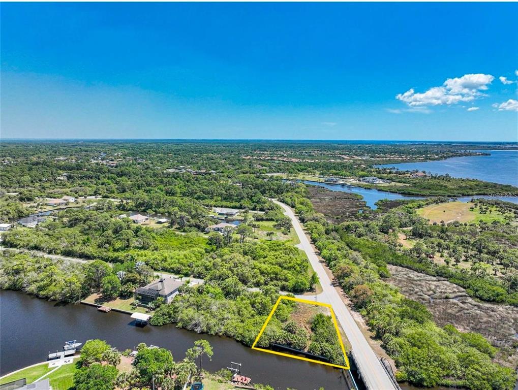 An aerial view shows a vacant waterfront lot outlined in yellow next to a road — 12412 EISENHOWER DRIVE, PORT CHARLOTTE, FL