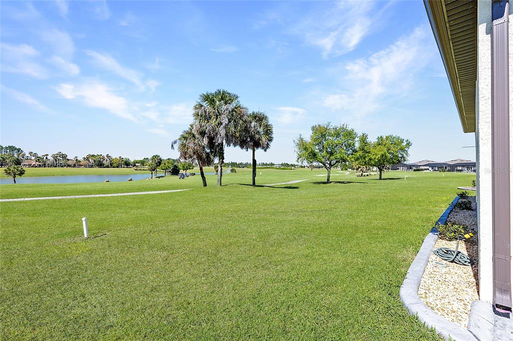 A grassy backyard overlooks a golf course with palm trees and a pond — 5702 SW 90TH COURT ROAD, OCALA, FL