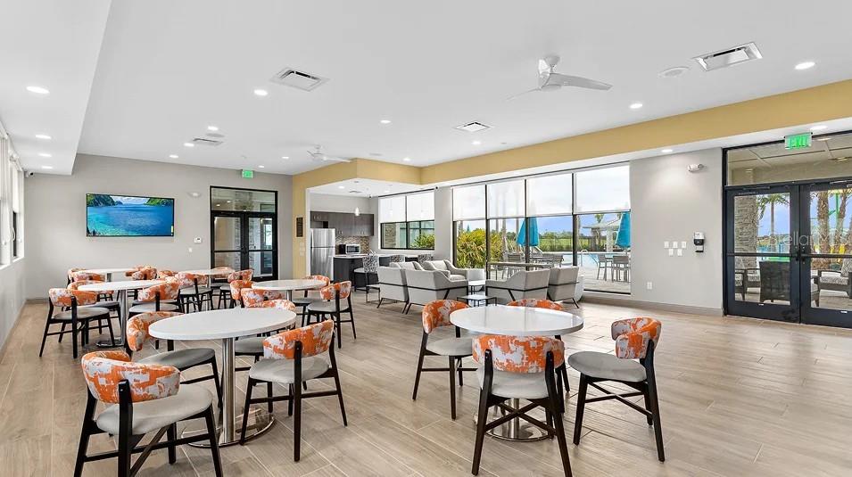 A bright, modern community room features multiple dining tables, chairs, and large windows overlooking outdoors — 522 OAK CREEK LANE, DAVENPORT, FL
