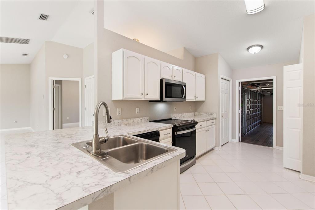 A kitchen with white cabinets, marble-look countertops, black appliances, and light tile flooring — 6294 ARBOREA DRIVE, INDIAN LAKE ESTATES, FL