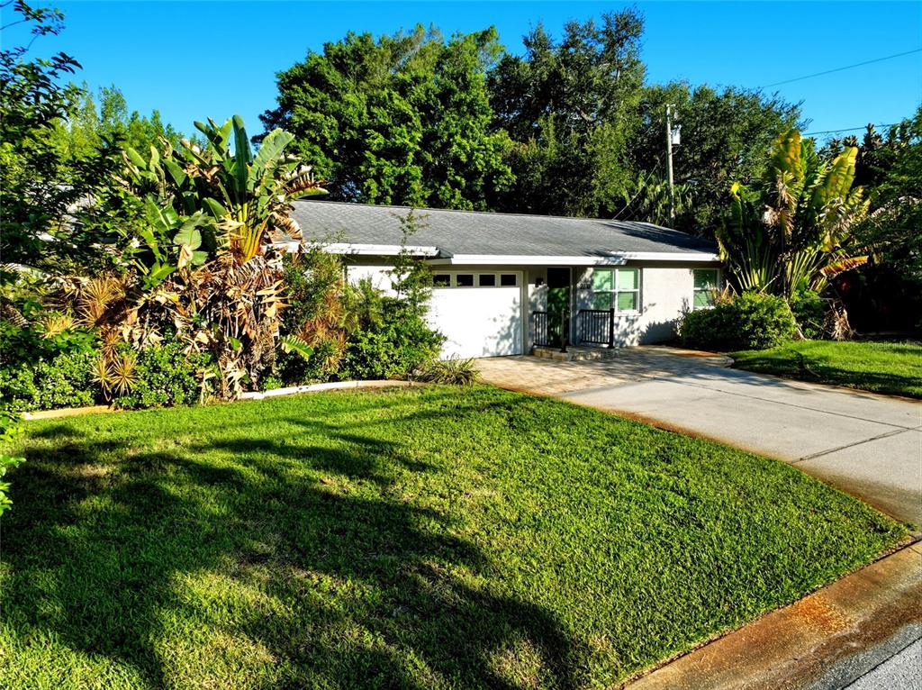 A single-story house with a white garage, paved driveway, and lush landscaping under a blue sky — 2310 29TH STREET N, ST PETERSBURG, FL