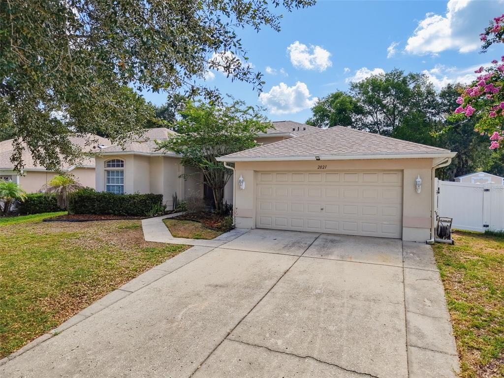 A single-story house with a beige stucco exterior, a two-car garage, and a concrete driveway — 2021 RUTHERFORD DRIVE, DOVER, FL