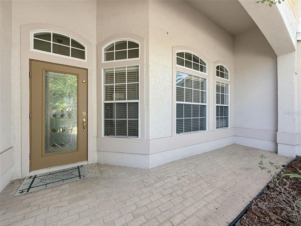 A tan front door with a glass insert sits beside three windows on a porch — 2021 RUTHERFORD DRIVE, DOVER, FL
