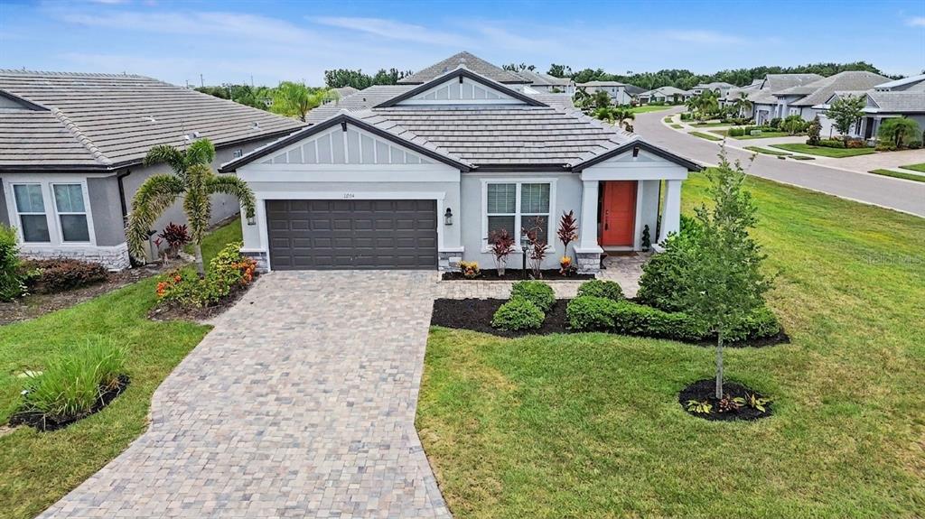 A single-story suburban house with a gray tiled roof, paver driveway, and orange front door — 12115 BALD CYPRESS COVE, PARRISH, FL
