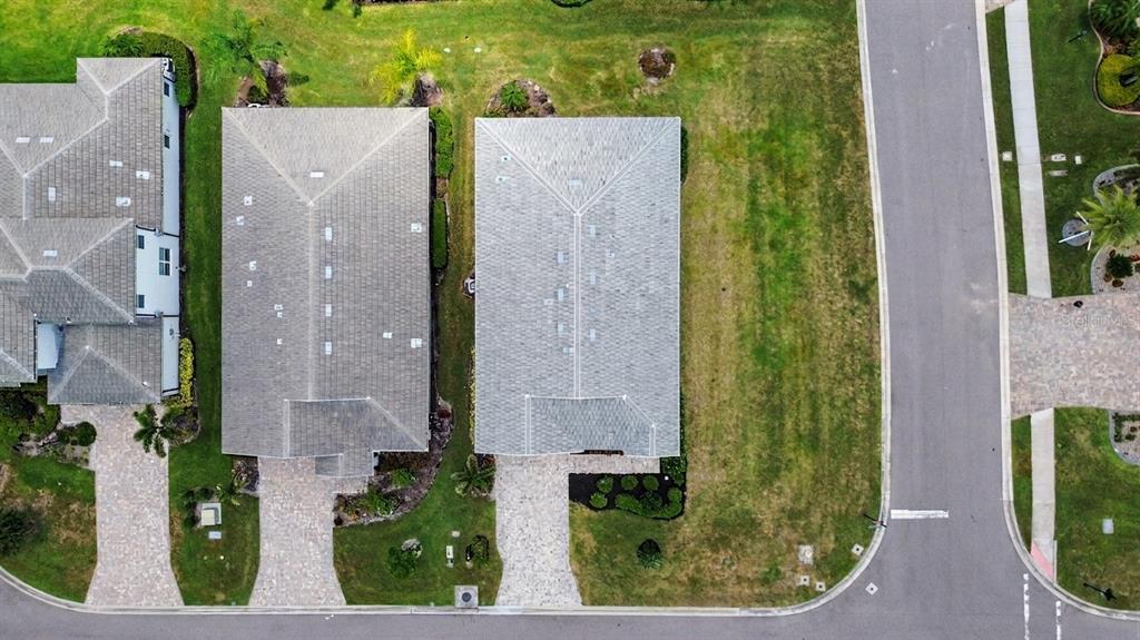 An aerial view shows two adjacent houses with gray roofs and paved driveways — 12115 BALD CYPRESS COVE, PARRISH, FL