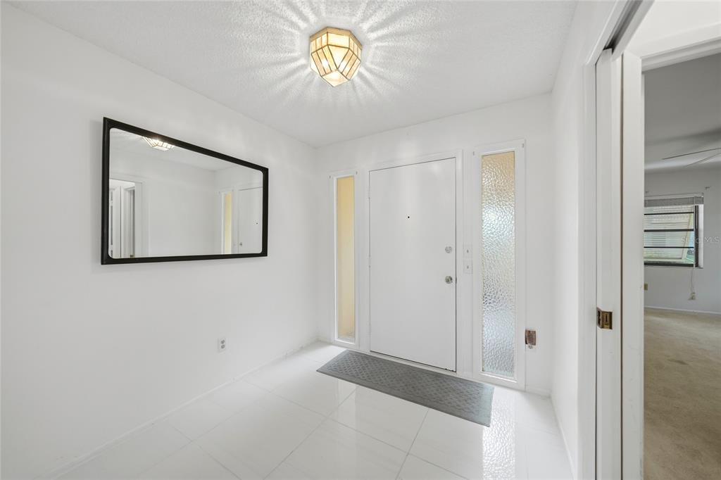 A bright entryway features white tile floors, a geometric ceiling light, and a large wall mirror — 49 SANDSTONE CIRCLE, VENICE, FL