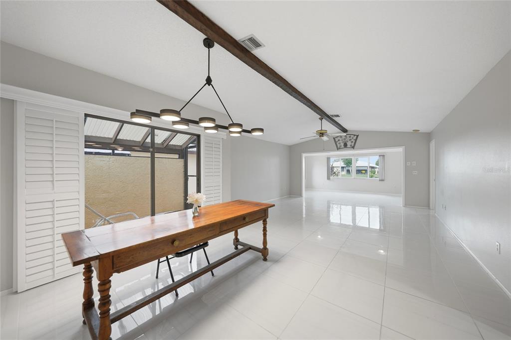 A dining area with a wooden table, modern chandelier, and tile flooring leads to a living room — 49 SANDSTONE CIRCLE, VENICE, FL