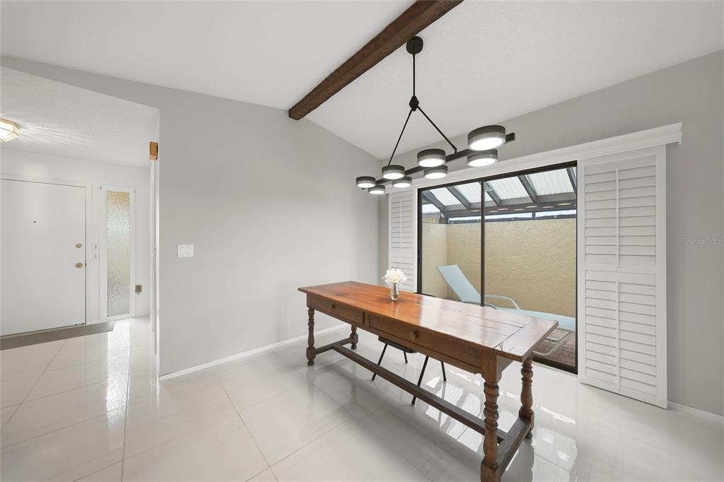 A dining room features a wooden table, a modern chandelier, and a sliding glass door — 49 SANDSTONE CIRCLE, VENICE, FL
